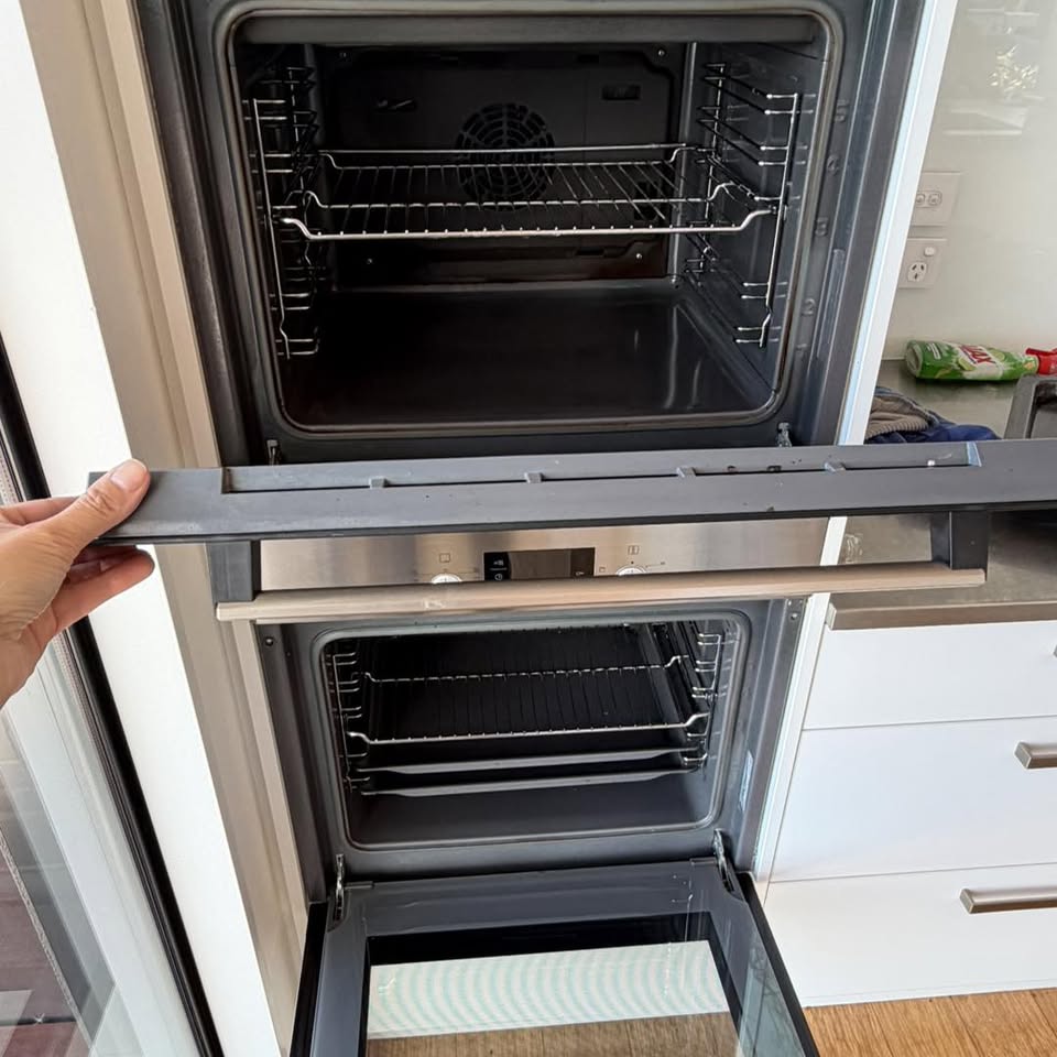 Kim holding a removed oven door panel, showing the thorough deep-clean method used on ovens, hobs and rangehoods